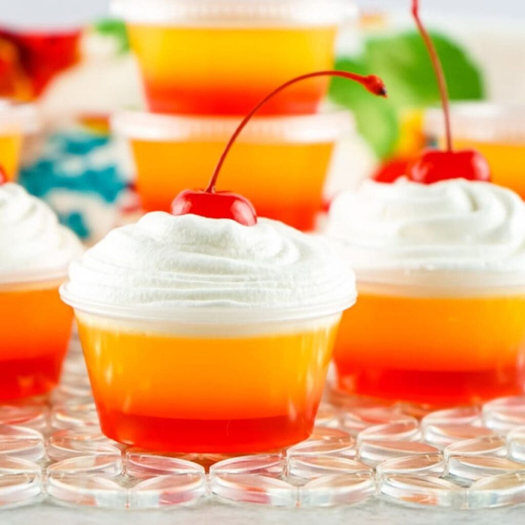 tequila sunrise jello shots with whipped cream and a cherry on top