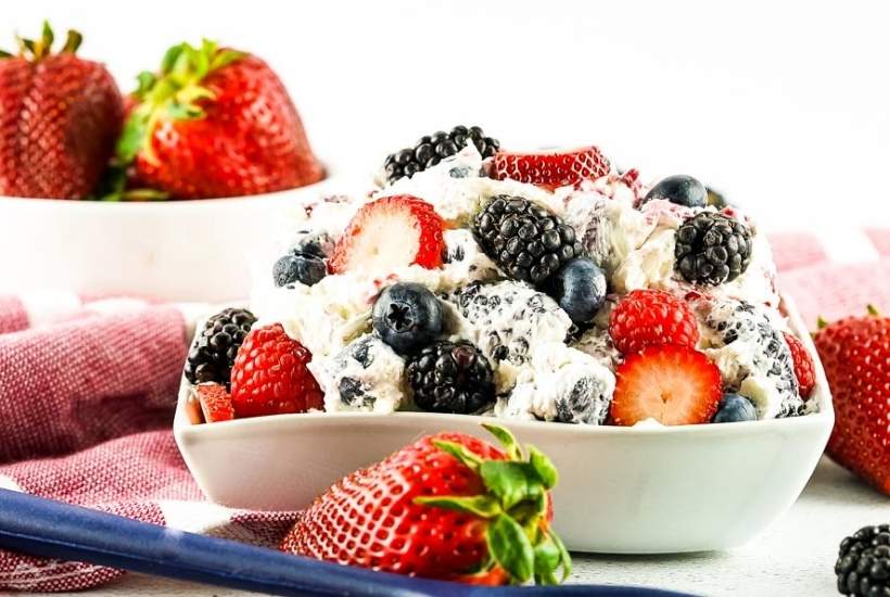 red, white, and blue cheesecake salad in a bowl next to whole strawberries
