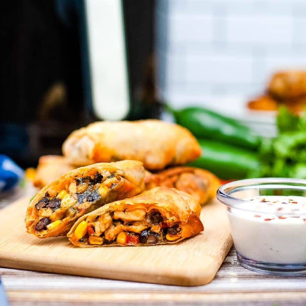 Air fryer southwest egg rolls on cutting board next to dipping sauce.