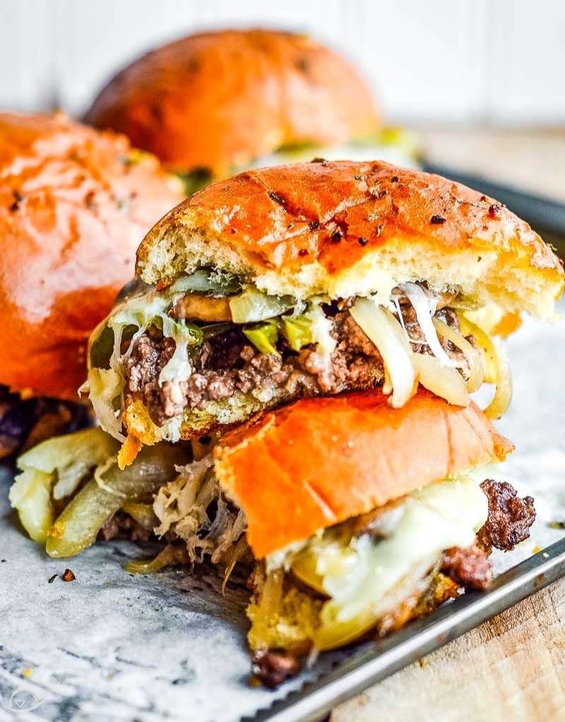 homemade ground beef Philly cheesesteak slider halves stacked on a baking sheet