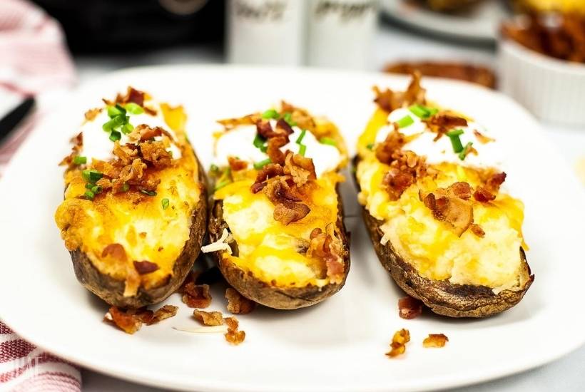 three twice baked potatoes topped with bacon and chives on a white plate