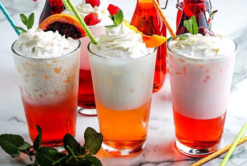 three homemade italian cream sodas with whipped cream, garnishes, and straws