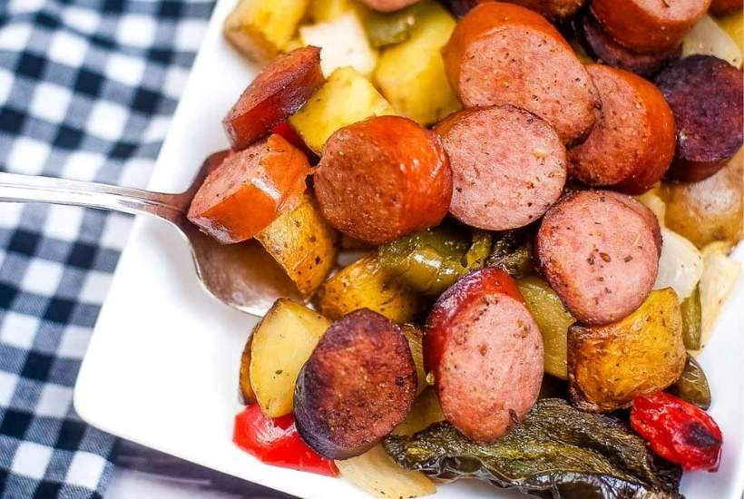 close up of cooked smoked sausage with vegetables on a white plate with a serving fork