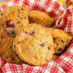 several raspberry oatmeal muffins in a basket with a red and white towel