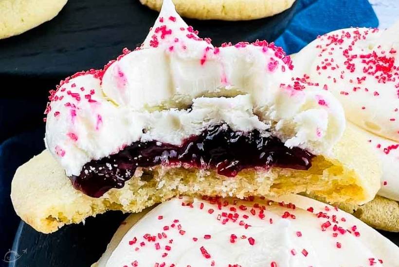 close up of a strawberry marshmallow cookies topped with pink sprinkles with a bite taken out.