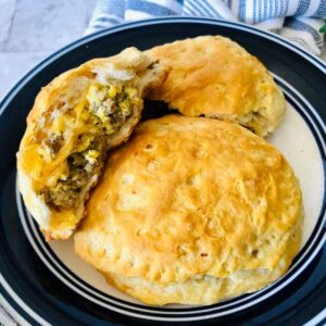 several stuffed breakfast biscuits on a plate with one that is cut in half