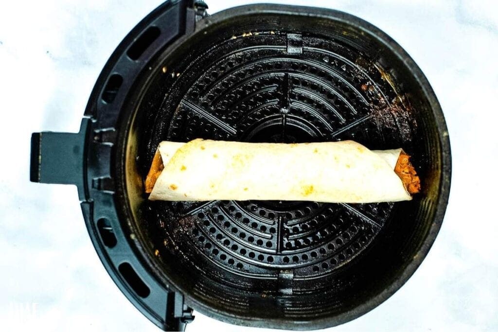 one chicken taquito in an air fryer basket