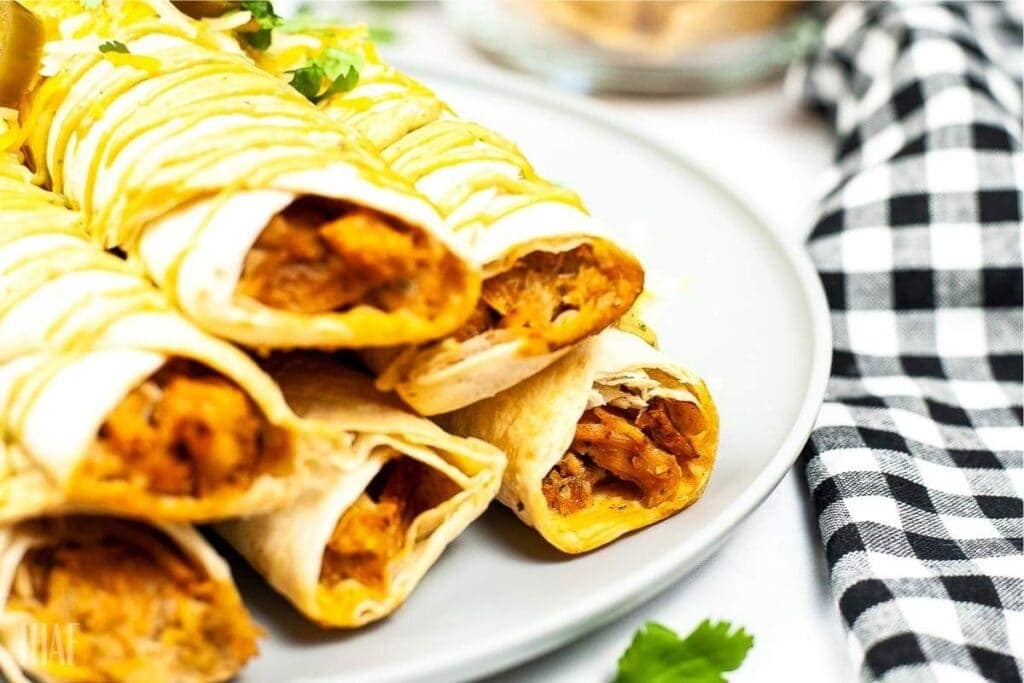 close up of stacked chicken taquitos that have been air fried and drizzled with sauce