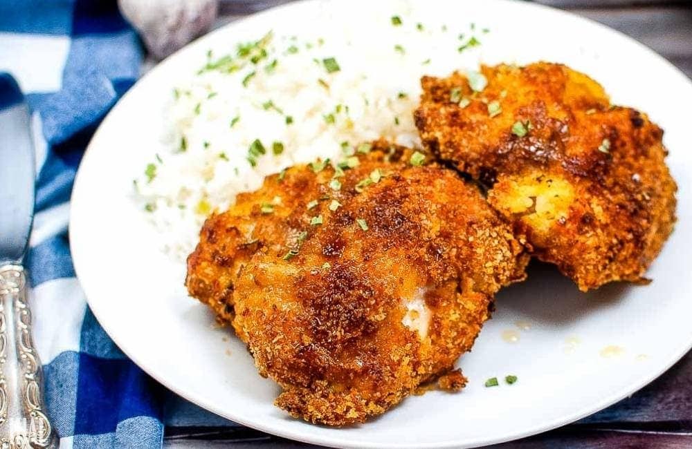 honey glazed air fryer chicken thighs with rice on a white plate next to blue plaid dish towel