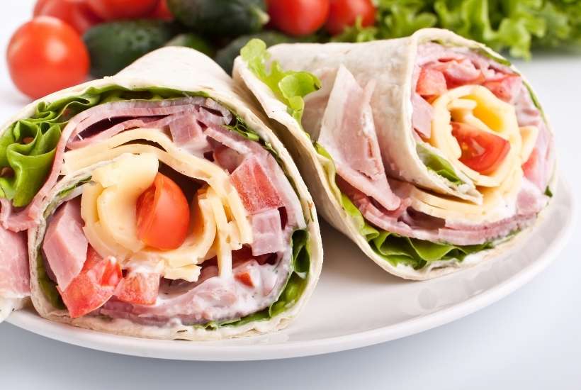 two ham and cheese wraps on a white plate