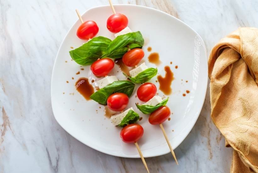 caprese skewers drizzled with balsamic on a white plate