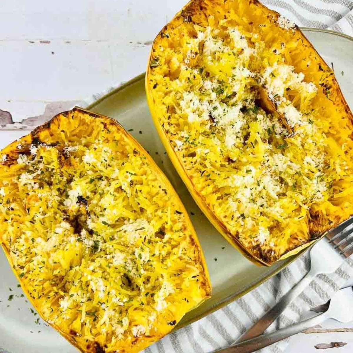 close up of two air fried spaghetti squash halves on an oval plate next to silverware.