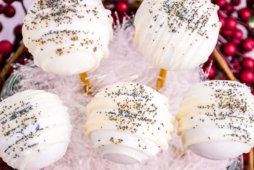 Gingerbread cake balls decorated with melted chocolate and silver sprinkles displayed in a container.