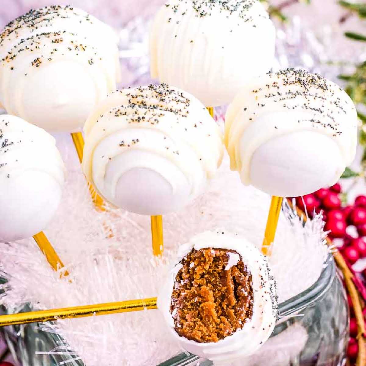 Closeup view of Gingerbread Cake Pops covered in white chocolate and decorated with sprinkles, with one with a bite removed.