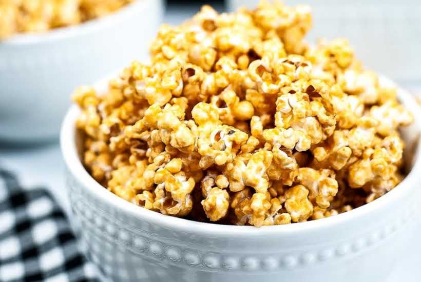Side view of easy homemade caramel popcorn in a white bowl next to white and black dish towel.