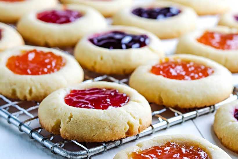 front close up of finished strawberry jam cookies and other flavors on wire cooling rack.