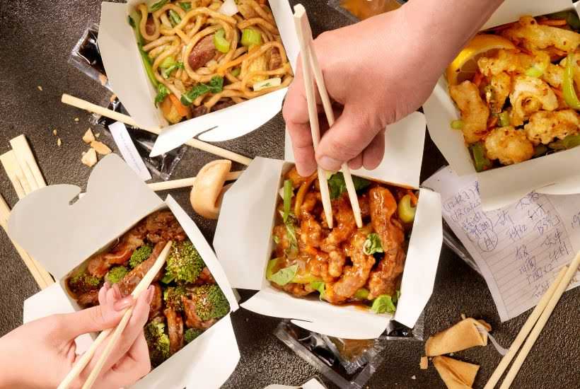 People eating with chopsticks out of Chinese to go boxes.