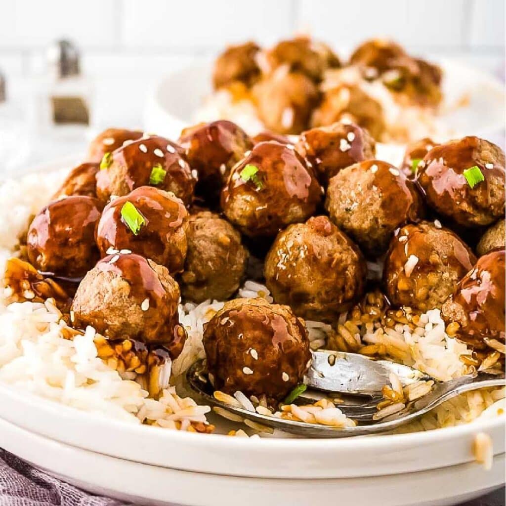 Teriyaki meatball bowls on a bed of rice next to a serving spoon.