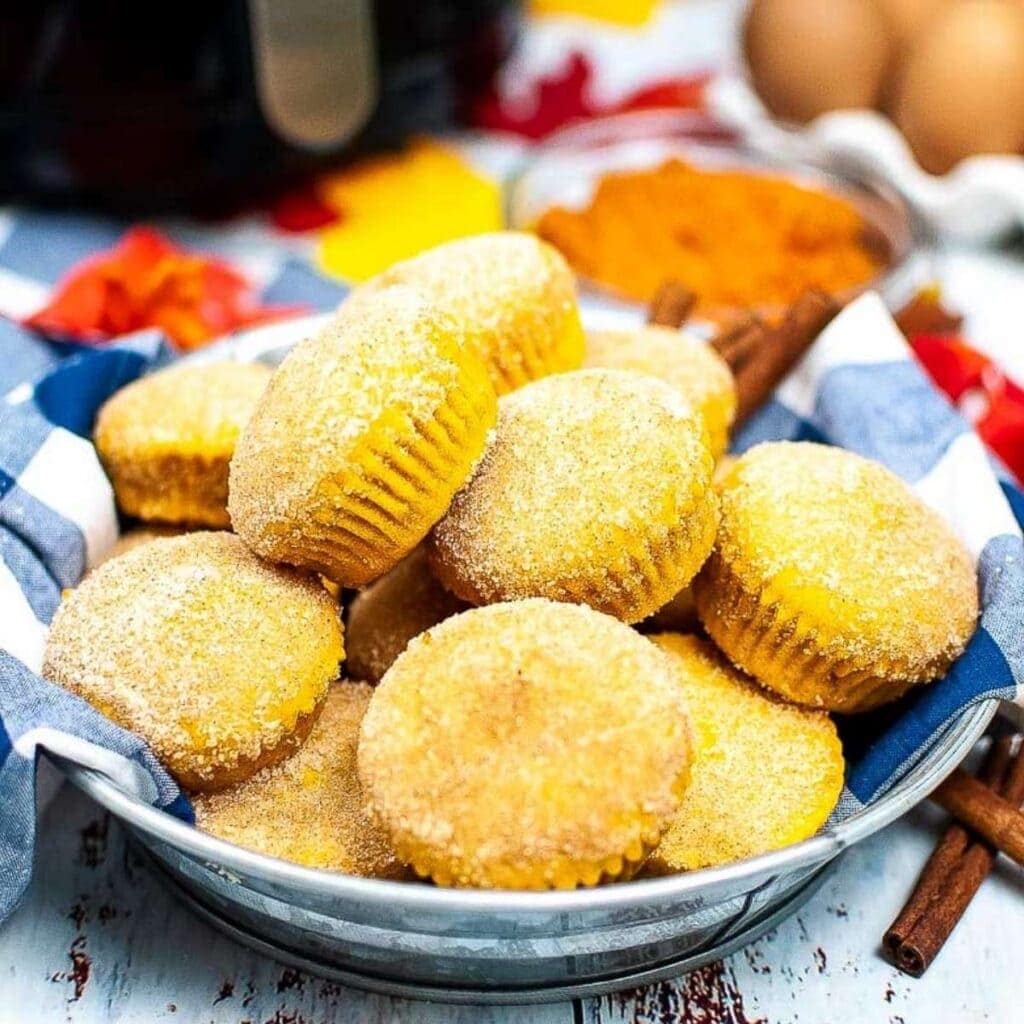 a batch of air fryer pumpkin muffins stacked in a cloth lined bowl.