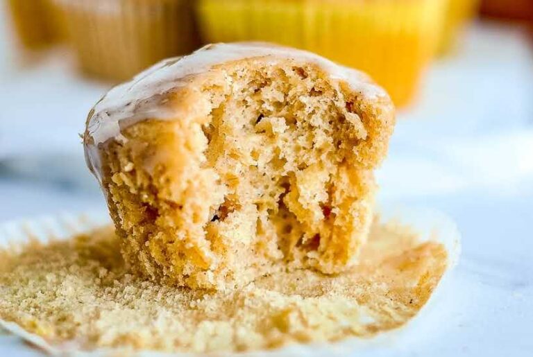 An unwrapped apple muffin with oats with a bite taken from it.