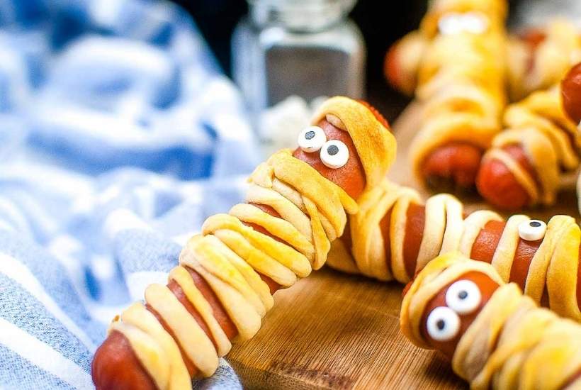 close up of a mummy dog with eyes laying on top of another next to a blue and white striped kitchen towel