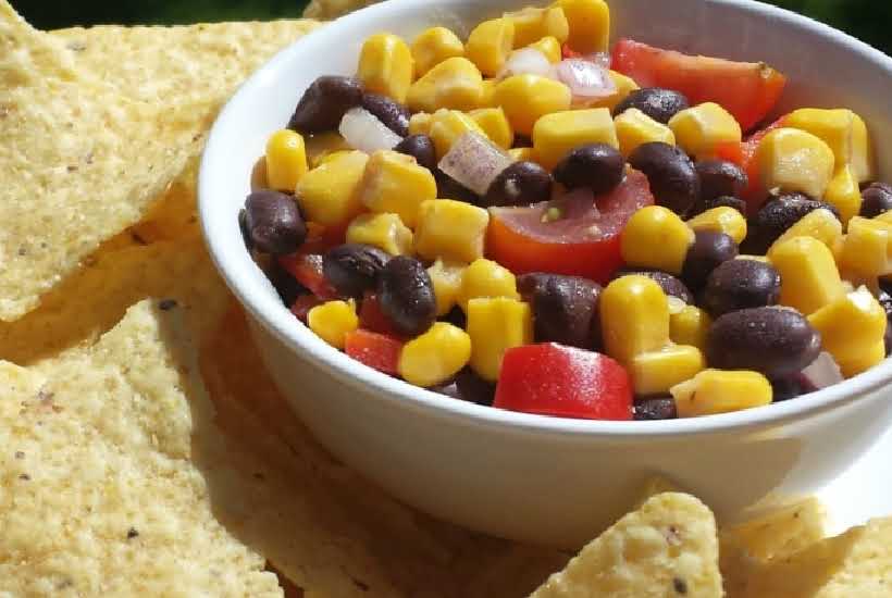 a white bowl filled with fiesta salad next to tortilla chips.