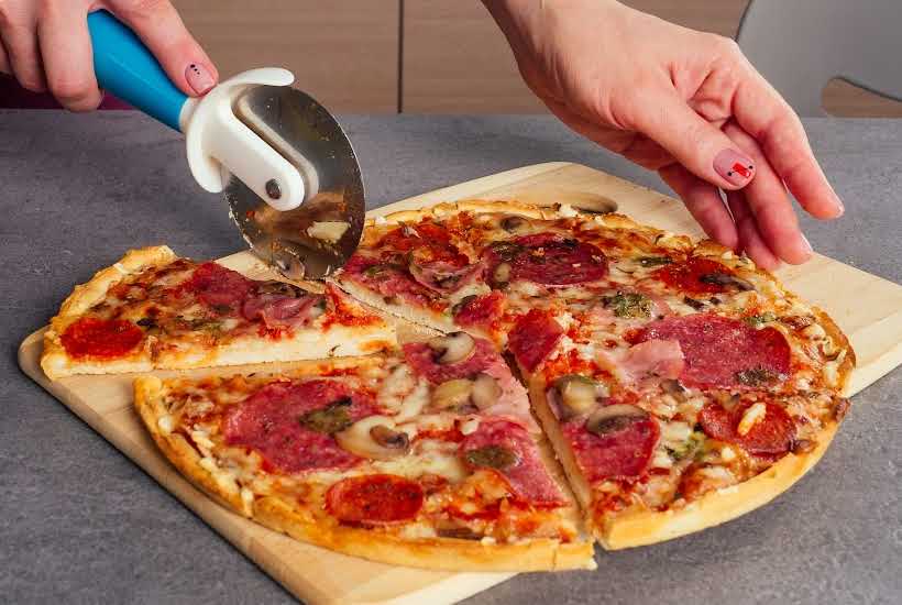 Slicing a pizza on a wood cutting board.