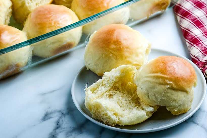 small plate with easy yeast rolls one split in half and a 9x13 pan full of them in the background.