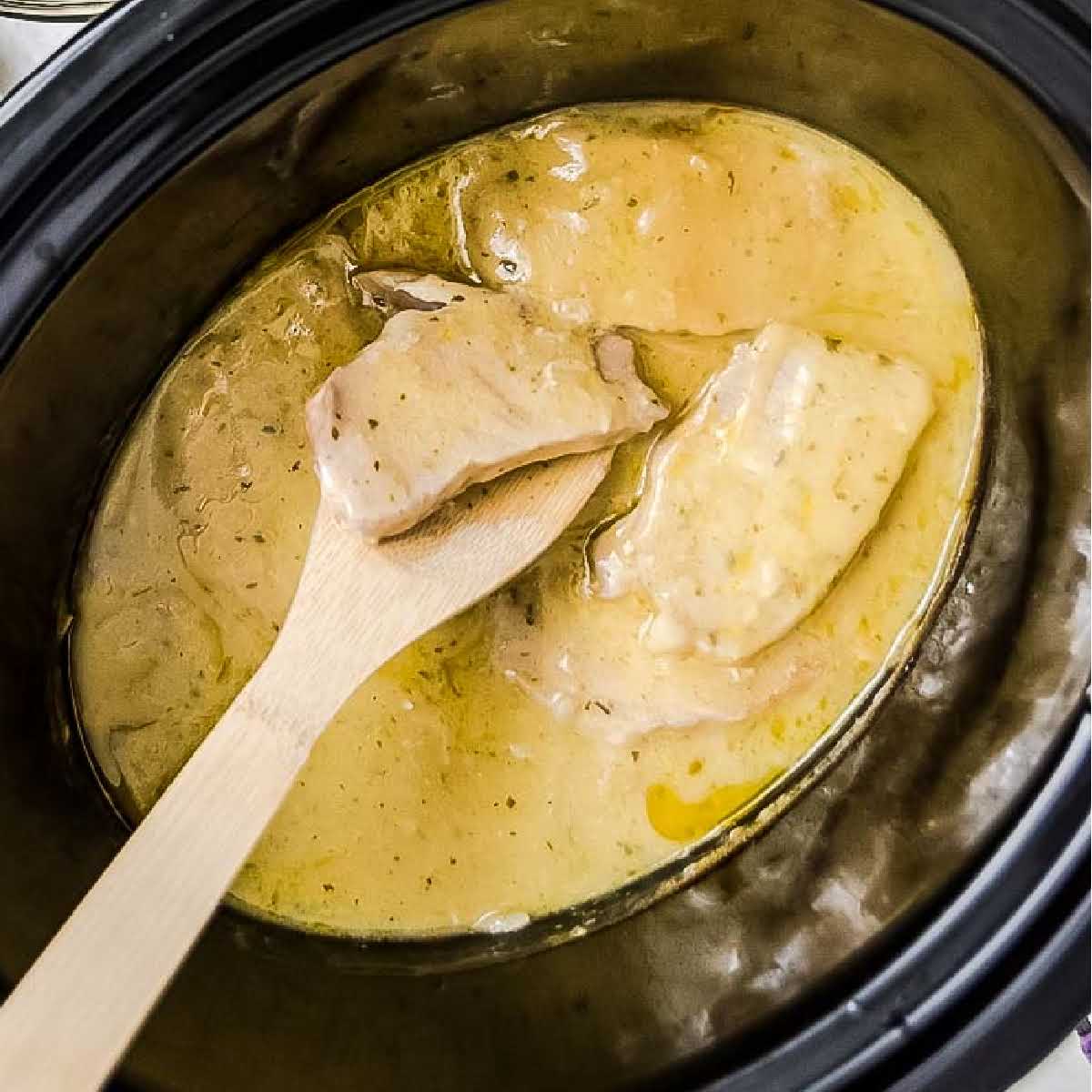 Ranch pork chops with gravy in a crockpot with a wooden spoon.