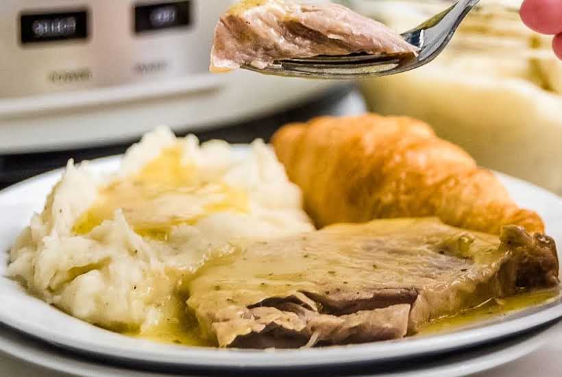 A white plate filled with ranch pork chops, mashed potatoes and bread with a bite of meat on a fork.