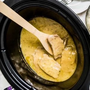 Cooked ranch pork chops in a black crockpot with a wooden spoon.