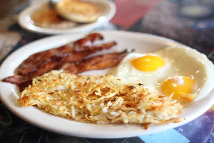 Fried eggs, bacon, and hashbrowns on a large white plate.