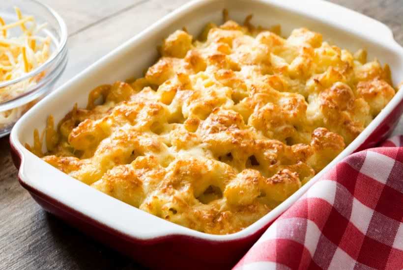 Baked mac and cheese in a casserole dish next to a red plaid towel.