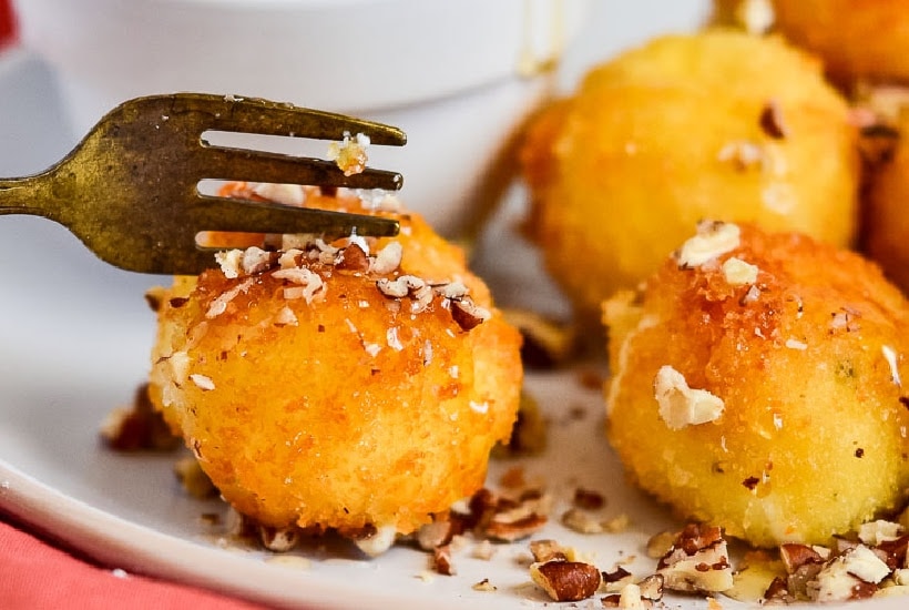 close up of fried goat cheese balls on a plate with a fork cutting into one.