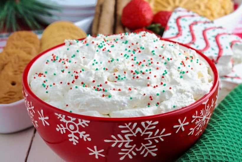 front view of red bowl filled with Christmas tree dip with dippers in the background.