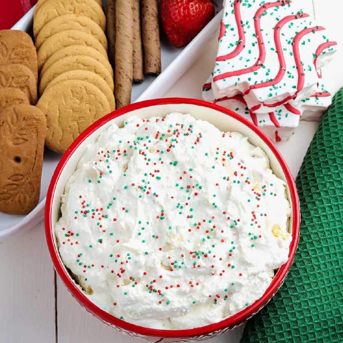 top view of red bowl filled with Little Debbie Christmas tree dip next to a platter of cookies and fruits.