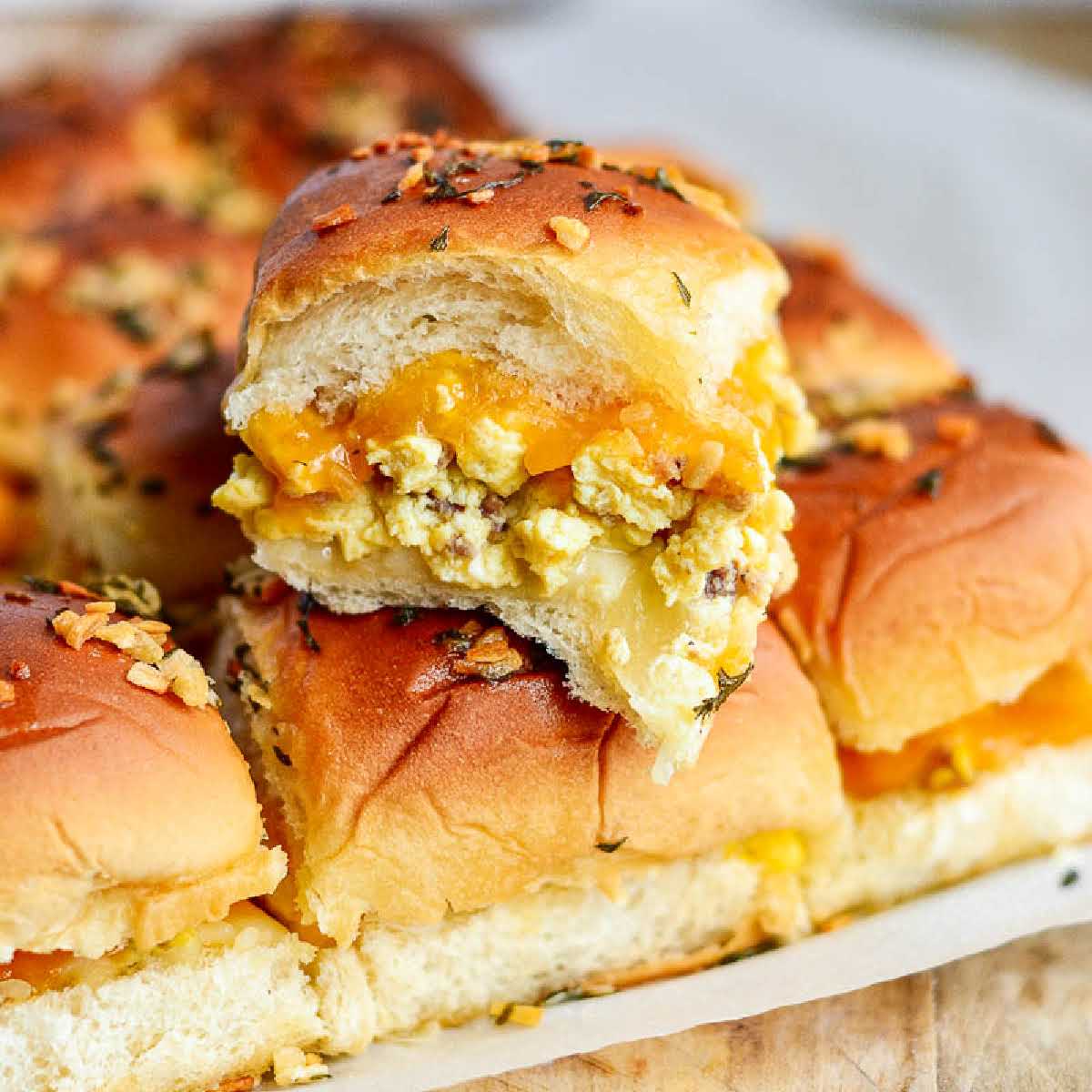 Hawaiian roll breakfast sliders on a parchment paper sheet with a closeup on one slider.