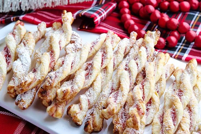 Close up of raspberry pastry twists on a white platter with red decor in the background.