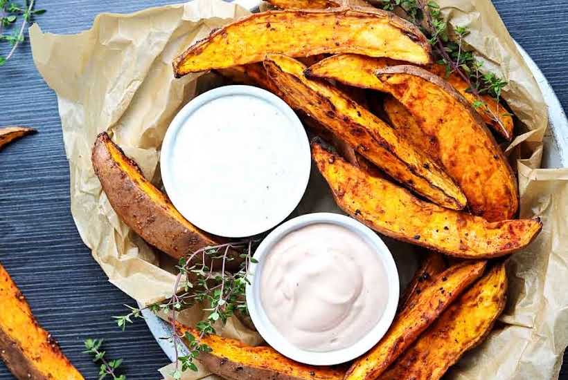 top view of sweet potato wedges with two white bowls filled with dipping sauces.