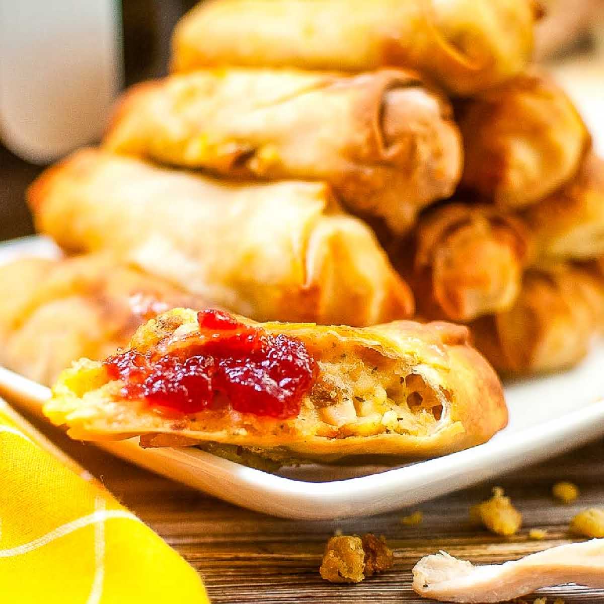 close up of half of a Thanksgiving egg roll with cranberry sauce and more piled up on a white plate. 