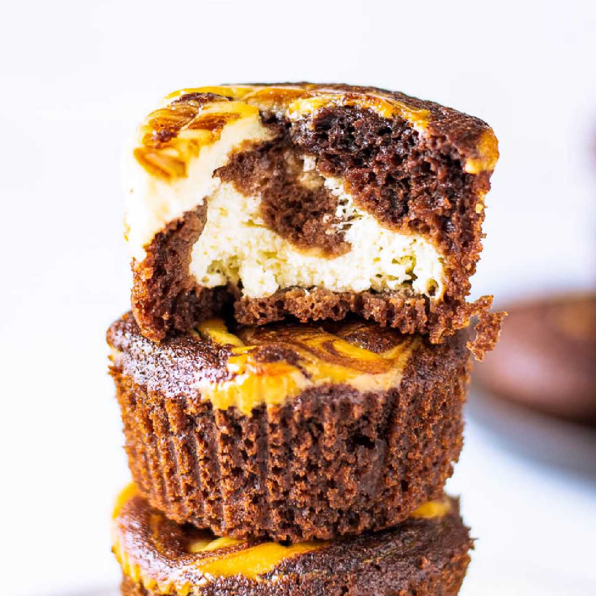 close up of stacked chocolate cream cheese muffins with a bite from the top one.