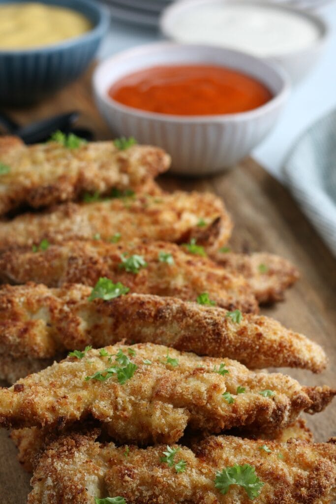 easy pantry meals of breaded chicken tenders on a wooden cutting board with dipping sauces in the background.