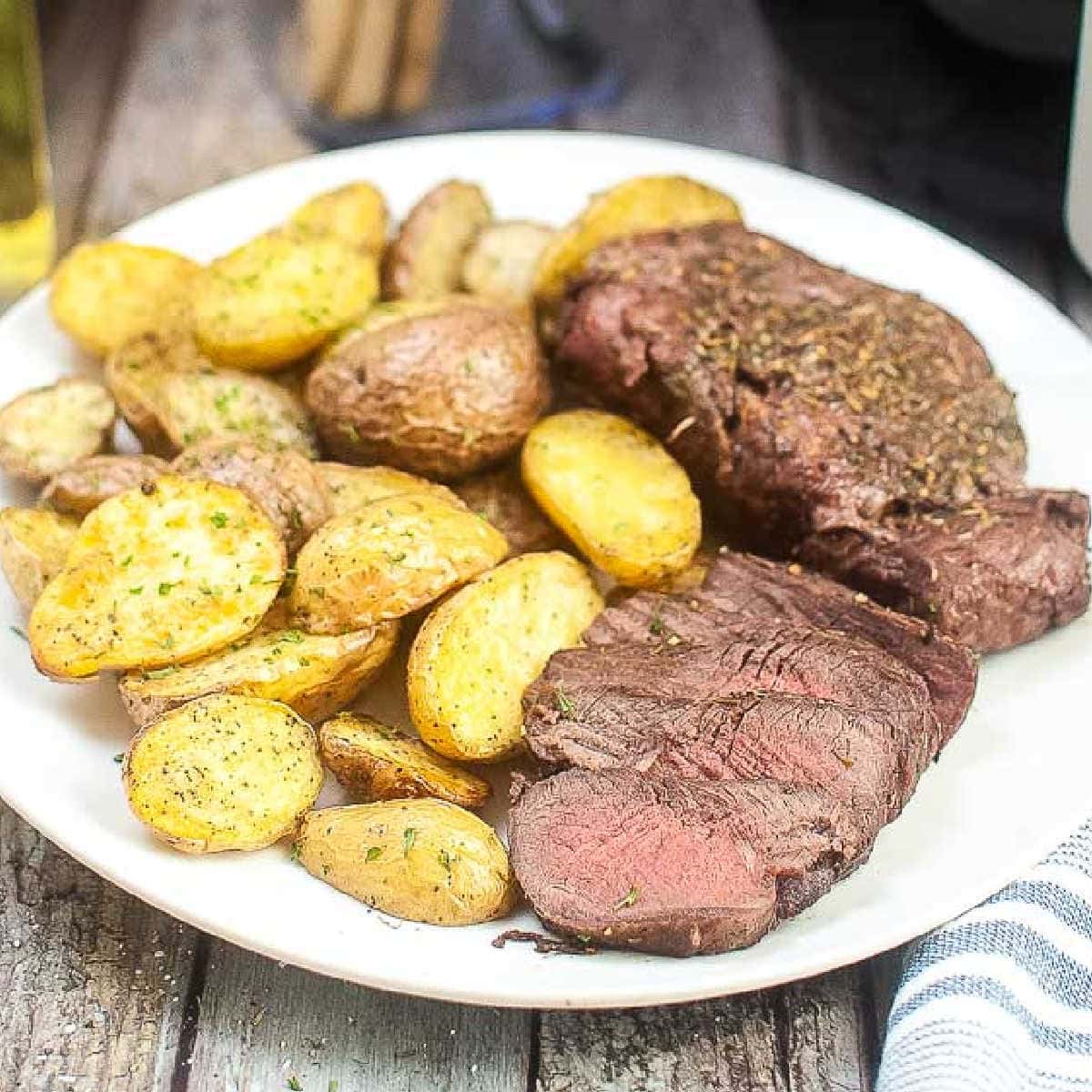 close up view of sliced air fryer filet mignon and potatoes on a white plate.