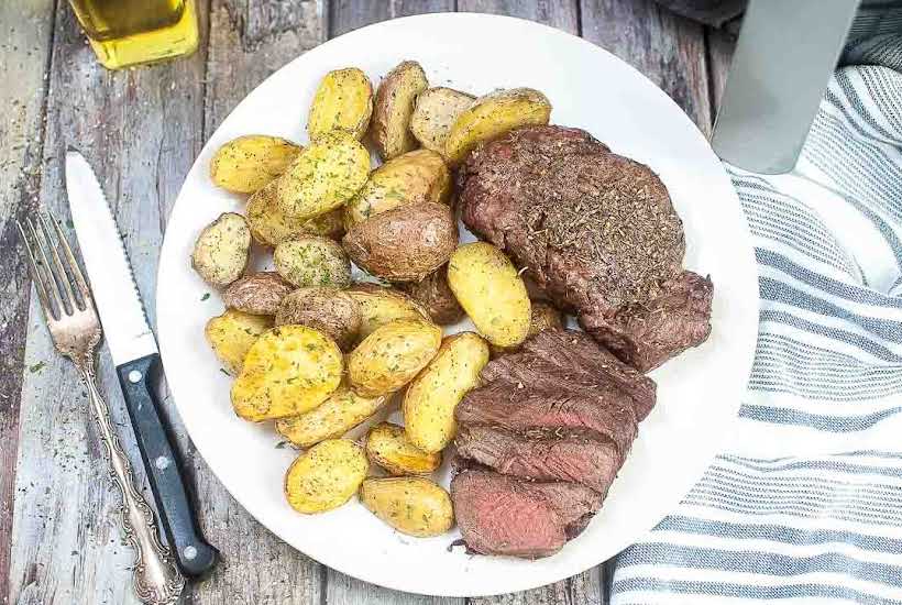 top view of air fryer steak and potatoes on a white plate next to a fork and knife.