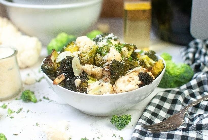 a bowl of roaste broccoli and cauliflower in a white bowl next to a fork and napkin.
