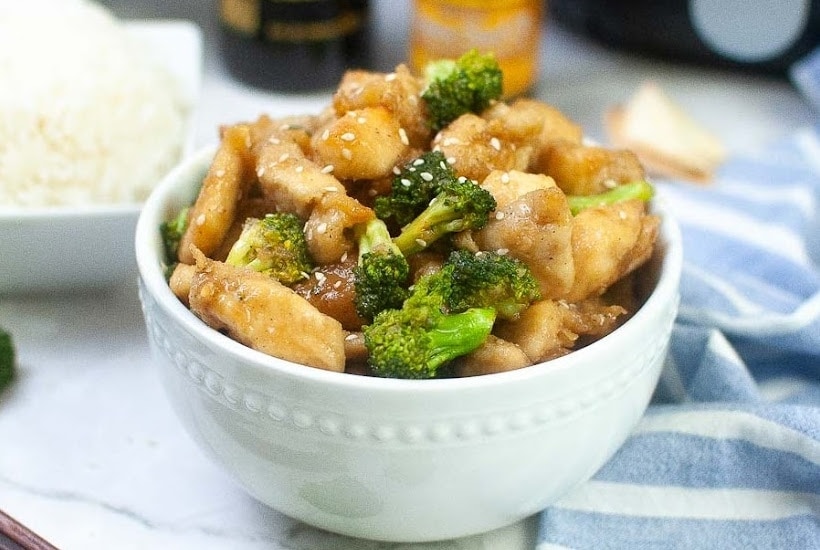 a white bowl filled with air fried chicken and broccoli.