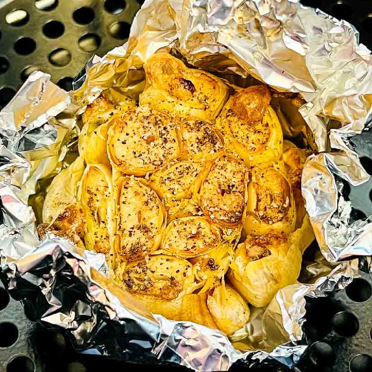 air fryer roasted garlic wrapped in foil in air fryer basket.