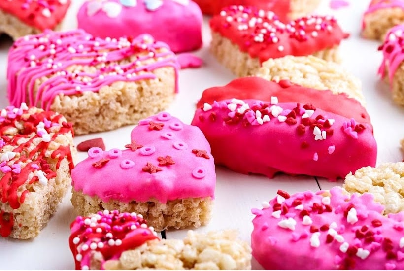 Valentine rice krispie treats with pink and red frosting topped with sprinkles.