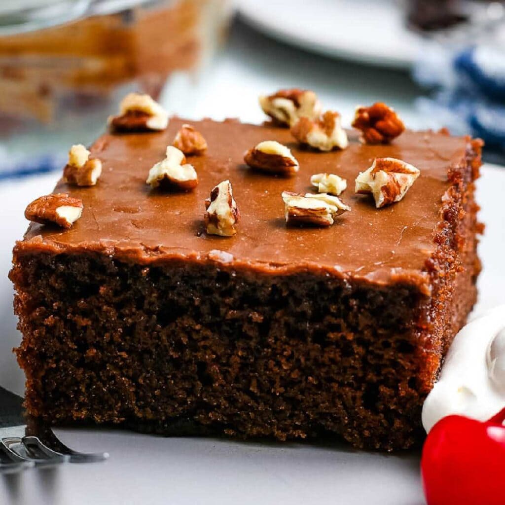 a slice of old fashioned coca cola cake topped with chopped nuts next to a cherry