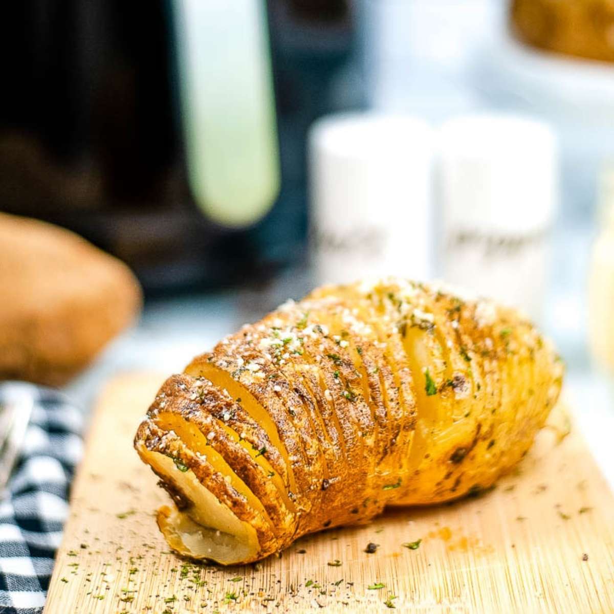 close up of an air fried Hasselback potato on a wooden cutting board.